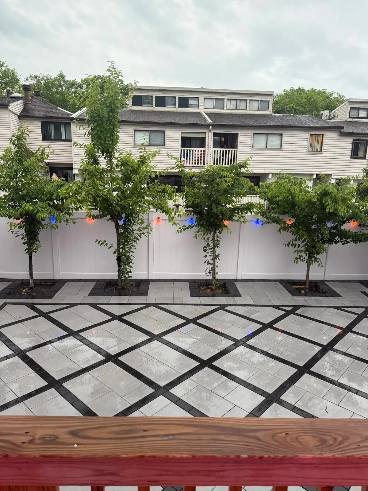 Gray paver patio with diamond pattern behind white fence and trees — APPLE MASONRY INC in Staten Island
