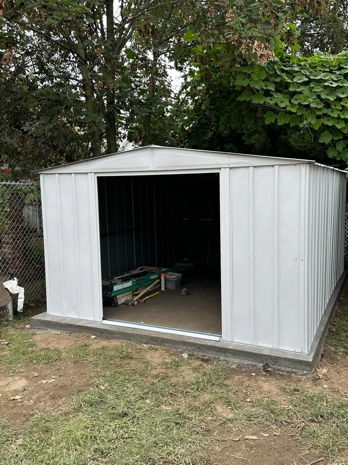 New white metal storage shed on concrete slab in yard — APPLE MASONRY INC in Brooklyn
