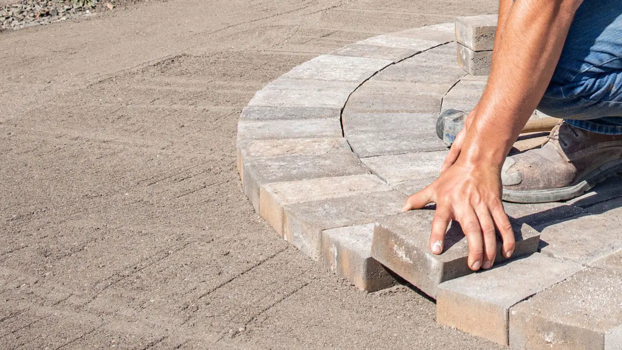 Hands placing circular paver course on compacted sand base — APPLE MASONRY INC in Brooklyn